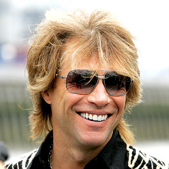 Bon Jovi - primo piano - capelli biondi scapigliati, occhiali grandi scruri, sorriso di un giovane spensierato.